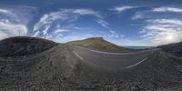 a fisheye image shows a curved road through the rocks and sand, looking over a mountain with a dirt hill on it