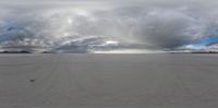 an icy lake with white sand and mountains in the background and a long line of tracks on it