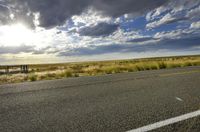 a road in a wide open field under cloudy skies with clouds on the horizon and the sky above it
