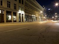 an empty city street with the lights on and cars parked along one side of the road