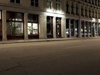an empty city street with the lights on and cars parked along one side of the road