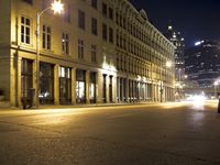 an empty city street with the lights on and cars parked along one side of the road