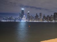 a city skyline, with water and sand near it at night with a bench by the waterfront