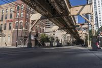 city street with buildings and a bridge above it and pedestrian on the sidewalk next to building