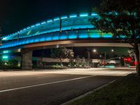 an illuminated bridge over the street at night in a city area with no traffic at all