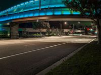 an illuminated bridge over the street at night in a city area with no traffic at all