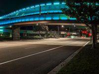 an illuminated bridge over the street at night in a city area with no traffic at all