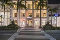 a lighted shopping center on a quiet day at night with palm trees in the front