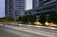 a street lined with tall buildings and trees at night time time near a road with street lights