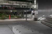 the empty entrance of the building is illuminated at night with lights on, and a ramp is leading to a large building