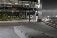 the empty entrance of the building is illuminated at night with lights on, and a ramp is leading to a large building