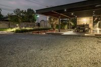 the outside of a home with a patio lit up at night, including a bench, gravel and fire pit