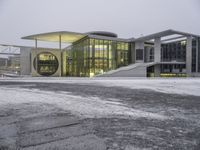 a bus drives in front of an impressive building in the snow, with lots of it's windows and concrete