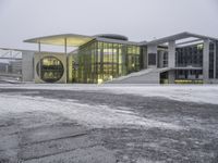 a bus drives in front of an impressive building in the snow, with lots of it's windows and concrete