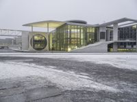 a bus drives in front of an impressive building in the snow, with lots of it's windows and concrete