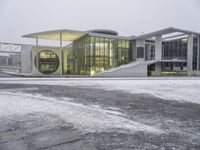 a bus drives in front of an impressive building in the snow, with lots of it's windows and concrete