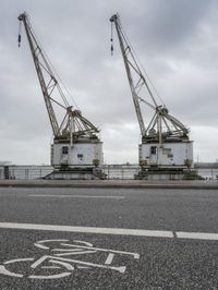 a bicycle lane has two large cranes standing over each other on it, with a bicycle painted on the side of the road