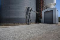 there is a cement walkway to an industrial area that holds several siloshes and storage units