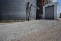 there is a cement walkway to an industrial area that holds several siloshes and storage units