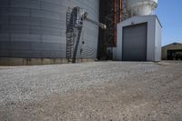 there is a cement walkway to an industrial area that holds several siloshes and storage units