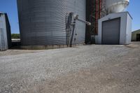 there is a cement walkway to an industrial area that holds several siloshes and storage units
