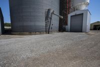 there is a cement walkway to an industrial area that holds several siloshes and storage units