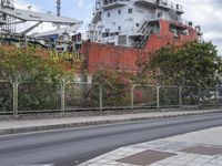 a large ship sitting behind a chain link fence on a street corner with another boat in the background