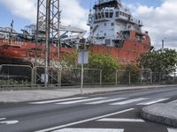 a large ship sitting behind a chain link fence on a street corner with another boat in the background