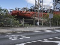 a large ship sitting behind a chain link fence on a street corner with another boat in the background