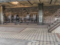 several machines and pipes are on a tile floor in a brick structure with iron staircases