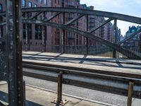 an industrial steel bridge over a roadway with buildings in the background with sunlight casting shadows of the bridge