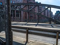 an industrial steel bridge over a roadway with buildings in the background with sunlight casting shadows of the bridge