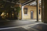 an empty dark street at night with lights on the building behind it and one side is empty
