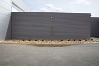 the wall is painted gray with a border of gravel and trees around it in front of an industrial building