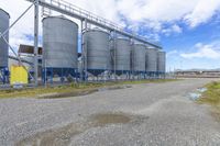 several steel tanks are lined up next to each other on gravel with clouds and blue sky