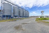 several steel tanks are lined up next to each other on gravel with clouds and blue sky