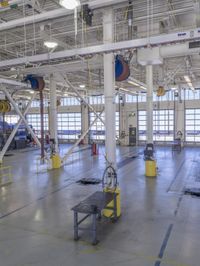 workers stand in a large industrial building with high ceilings and steel beams and pipes and a table