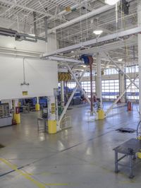 workers stand in a large industrial building with high ceilings and steel beams and pipes and a table