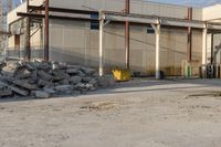 a bunch of rocks and piles of concrete in front of an industrial building on the street