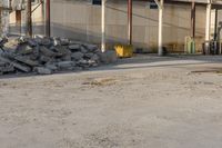 a bunch of rocks and piles of concrete in front of an industrial building on the street