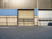 a street in front of an industrial building with roller shutter doors with shadow on it