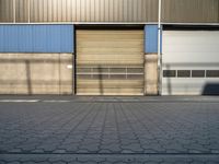 a street in front of an industrial building with roller shutter doors with shadow on it