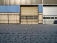 a street in front of an industrial building with roller shutter doors with shadow on it