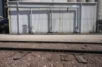 several steel containers sit next to a railroad track and buildings on a sunny day outside