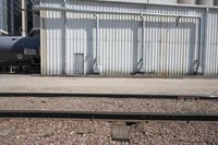 several steel containers sit next to a railroad track and buildings on a sunny day outside