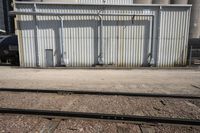 several steel containers sit next to a railroad track and buildings on a sunny day outside