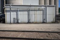 several steel containers sit next to a railroad track and buildings on a sunny day outside