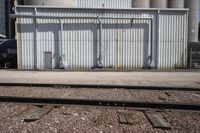 several steel containers sit next to a railroad track and buildings on a sunny day outside