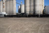 two trucks parked next to large cement silos near another building with large silos behind it