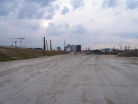 a dirt road in an empty city during the day time with clouds above it's tops